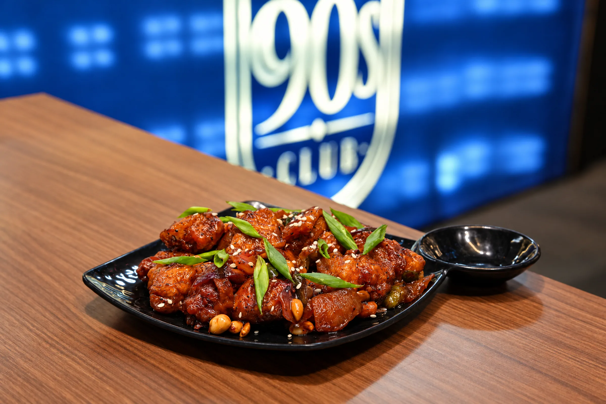 Chilli Chicken with spring onion and sesame on a black plate at The 90s Club, Electronic City.