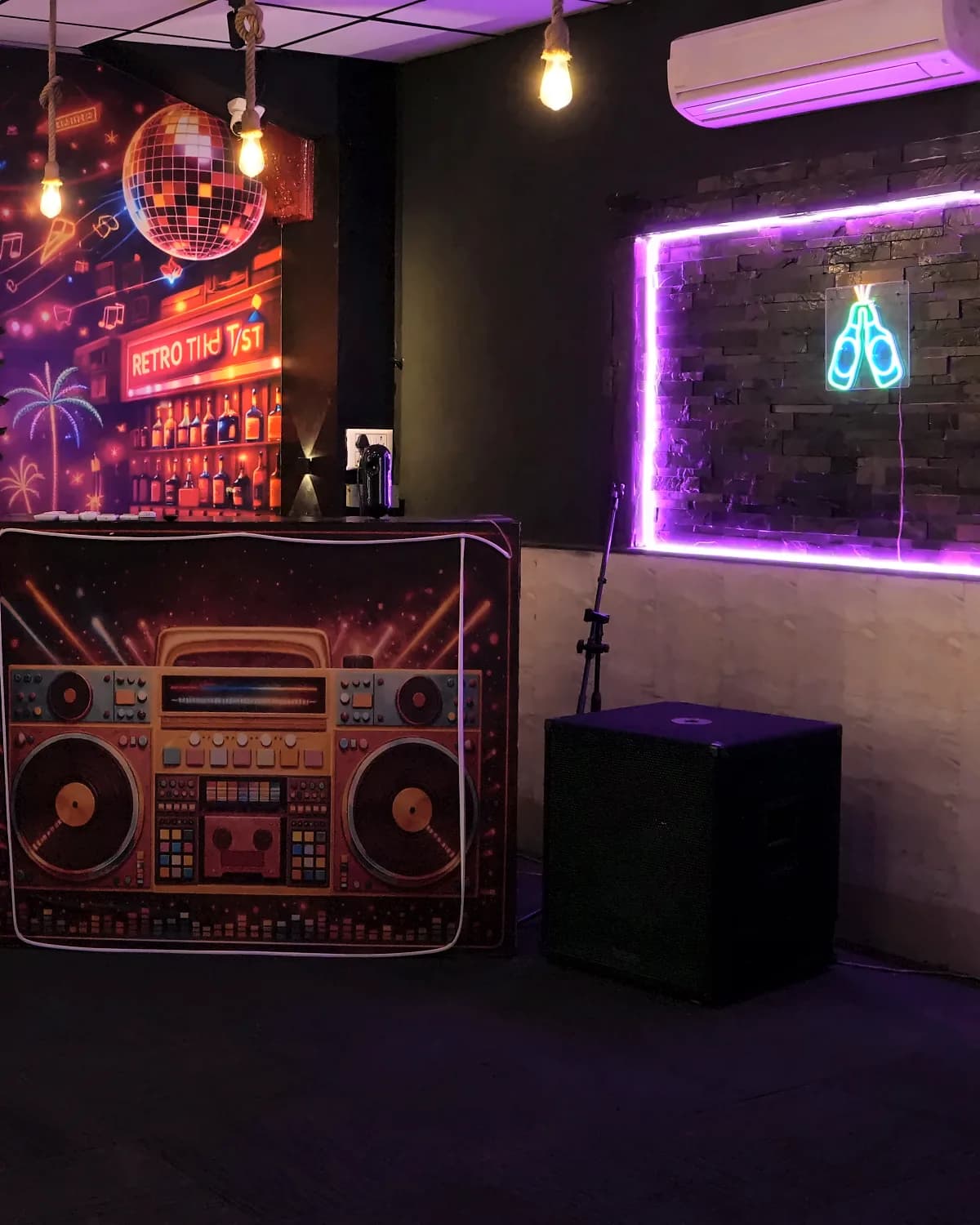 A boombox-print DJ booth, a disco-ball mural and a purple neon wall in the music corner of The 90s Club, Electronic City.