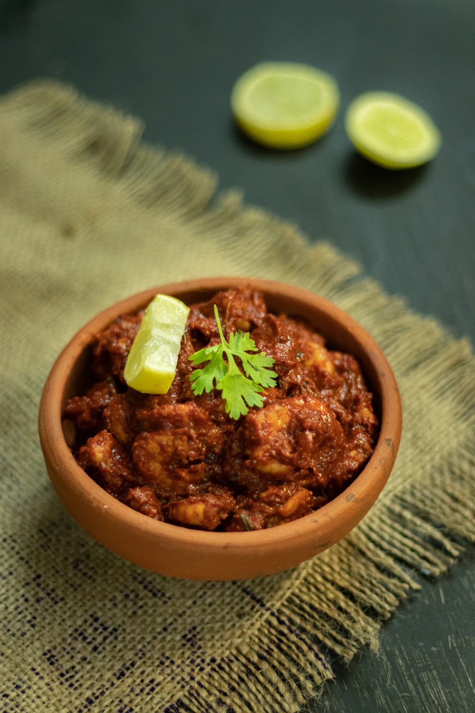 Chicken ghee roast in a clay bowl with a wedge of lime and coriander.